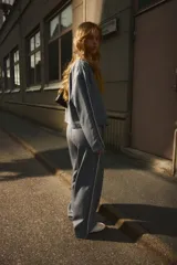 Pantalón de vestir gris oscuro con finas rayas verticales blancas (pinstripe), tiro alto y cintura elástica con cordón blanco ajustable. Presenta un corte ancho y recto, con una fina franja blanca lateral que recorre la pierna.