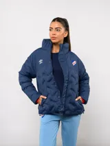Campera puffer corta de Umbro para el Club Nacional de Football, color azul marino con diseño termosellado. Cuenta con cuello alto, cierre frontal con botones a presión, bolsillos laterales y logo de la marca junto al escudo del club en el pecho.