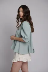 Chaqueta o blusa de tejido natural color verde menta, con mangas balloon y un botón decorativo en forma de estrella de mar. El cuerpo tiene un ruedo evasé.