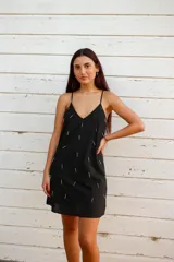 Vestido corto negro de algodón con breteles finos regulables y escote en V. Presenta bordados de canutillos y mostacillas plateadas. De corte holgado y forrado.