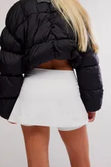 Skort deportivo blanco de tiro alto, con diseño cruzado en el frente y ribetes en contraste azul oscuro, que incluye short interno incorporado.