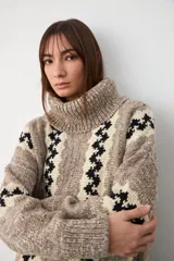 Sweater de punto con cuello tortuga, diseño holgado y estampado de rayas verticales con patrón geométrico en tonos beige, marrón y negro.
