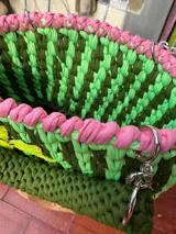 Cartera tejida a crochet en hilo de algodón color verde con detalles en rosa y aplique de flor amarilla con lentejuelas. Tiene doble asa corta y correa larga de cadena metálica.