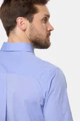 Camisa sport lisa de manga corta en color celeste, con cuello abotonado, cierre frontal con botones, bolsillo en el pecho y etiqueta decorativa en el ruedo.