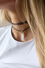 Gargantilla de cuero negro con dije de piedra blanca en forma de lágrima con engarce dorado.