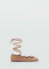 Zapato plano tipo chatita color nude, confeccionado en cuero, con diseño de tiras cruzadas y cordones para atar alrededor del tobillo, ojalillos metálicos dorados y punta redonda.