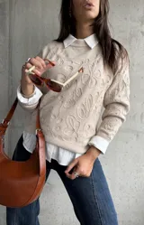 Sweater de punto color beige con diseño floral en relieve, cuello redondo y mangas largas. Presenta puños y ruedo acanalados.
