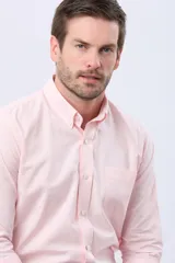 Camisa Oxford lisa de color celeste, con cuello abotonado, manga larga, cierre frontal de botones y un bolsillo aplicado en el pecho con detalle bordado.