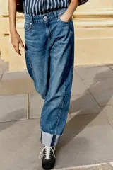 Jeans baggy de tiro medio con pernera holgada, diseño de cinco bolsillos y bajo acabado en vuelta. Cuenta con cintura elástica en la espalda y cierre frontal con cremallera y botón.