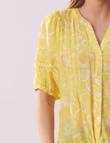 Blusa amarilla estampada con cuello en V, manga corta con volados y ruedo anudado.