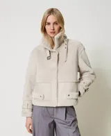 Chaqueta color beige de napa y piel sintética con cuello con cierre de hebilla y almeja, mangas largas con hombros caídos, tirantes en los puños, cierre de cremallera oculta, bolsillos laterales, cierre de hebilla y almeja en el dobladillo y placa en T ovalada en la parte posterior.