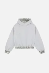 Hoodie cropped de Scuffers en color gris melange, con diseño oversized y detalles distressed. Presenta terminaciones con estampado animal print en la capucha, los puños y la cintura, e incluye un bolsillo frontal tipo canguro.