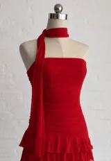Vestido corto rojo con escote strapless y detalle de choker integrado. Presenta un diseño ajustado en el torso con falda de volados y una tira lateral larga decorativa.