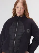 Campera crop de corte boxy y color negro, forrada en corderito, con parches capitoneados en el pecho y las mangas. Cuenta con cierre frontal metálico, cuello alto, puños y bajo elastizados, y detalle de logo bordado en hilo en el pecho.
