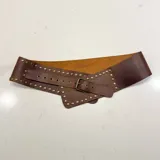 Cinto faja ancho de cuero genuino color marrón, con diseño de inspiración ecuestre y detalles de tachas metálicas en todo el contorno. Cuenta con una hebilla metálica central y cierre ajustable.