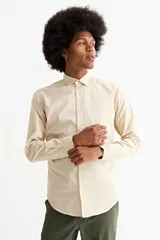 Camisa de manga larga en color beige, confeccionada en algodón, con cuello clásico y cierre frontal de botones.