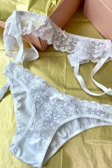 Conjunto de lencería compuesto por una bombacha de tiro medio y un portaligas, ambos confeccionados en encaje blanco con detalles de puntilla y pequeños lazos decorativos.