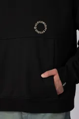 Buzo canguro oversize de frisa de algodón premium en color azul grisáceo. Presenta un diseño con recortes frontales, bolsillo tipo canguro y un pequeño logo circular estampado en el pecho. Cuenta con puños y ruedo acanalados.