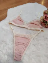 Conjunto de lencería compuesto por un bralette triangular y una tanga, confeccionados en algodón color rosado con detalles de encaje en tono crema. El bralette cuenta con breteles ajustables y el conjunto presenta terminaciones delicadas.