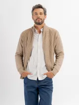 Campera tejida de punto en color beige, con diseño de trenzas y rombos, cuello alto y cierre frontal completo.