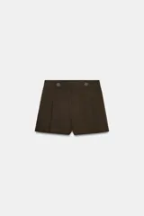 Short de tiro alto color marrón, con pliegues frontales y detalle de botones decorativos en la cintura. Cuenta con bolsillos laterales y cierre frontal con cremallera y gancho metálico.