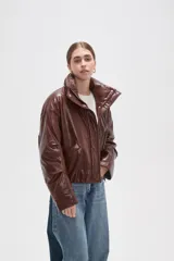 Campera de eco-cuero color marrón con cuello alto, cierre frontal oculto y bolsillos laterales. Presenta un diseño acolchado con acabado brillante.