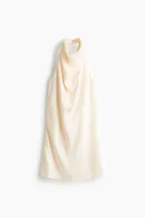 Minivestido de corte holgado en tejido fluido de satén color beige, con escote drapeado y tira halter con cierre de botones.