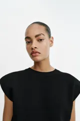 Top de punto negro con cuello redondo, manga sisa, hombreras marcadas y diseño ajustado con rib en el bajo.