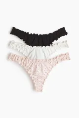 Pack de tres bombachas tipo colaless de tiro bajo con cintura en V y detalles de volados en los bordes. El set incluye una unidad negra lisa, una blanca lisa y una rosada con estampado de lunares pequeños.