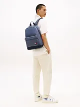 Mochila de diseño redondeado en color azul, confeccionada en poliéster. Cuenta con un compartimento principal con cierre de cremallera, un bolsillo exterior frontal con cierre, asa superior y correas acolchadas ajustables. Incluye parche distintivo de Tommy Jeans en la parte delantera.