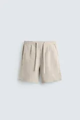 Bermuda de lino color blanco hueso, de corte relajado y tiro medio. Presenta cintura elástica ajustable con cordón, pliegues frontales y bolsillos laterales y trasero.