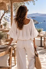 Blusa color beige confeccionada en lino, de diseño holgado y corto con cuello redondo elastizado que permite usarla estilo off-shoulder. Cuenta con mangas anchas y acampanadas con volados en capas.