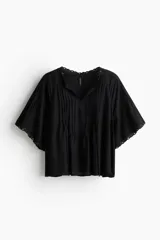 Blusa negra de tejido liviano con corte holgado, manga circular corta y escote en V con tiras finas ajustables. Presenta alforzas verticales en el frente y ojales metálicos decorativos en el escote y los bordes de las mangas.