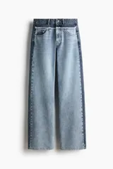 Jean de corte holgado y pierna recta confeccionado en denim de algodón rígido. Presenta un diseño bicolor con paneles en tonos contrastantes, costura desflecada en la cintura y franjas laterales. Cuenta con diseño de cinco bolsillos, cierre con botón y tachas metálicas con logo grabado.