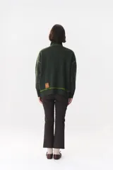 Campera de tejido de punto color marrón con destellos de lurex, corte oversize y cierre frontal. Presenta detalles de costuras y terminaciones en color crema, cuello alto y bolsillos frontales.