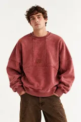 Buzo oversize de corte unisex, color rojo con efecto desgastado (acid wash), confeccionado en algodón con interior de polar. Presenta costuras frontales decorativas, hombros caídos, mangas largas con puños elastizados, rib en el cuello y el ruedo, y un pequeño logo bordado en el pecho.