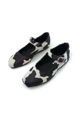 Zapato Mary Jane con estampado de vaca en blanco y negro, con correa al tobillo y hebilla plateada.