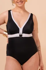Malla entera de traje de baño, color negro, con escote en V profundo ribeteado en blanco. Presenta un cinturón blanco que se une en el centro con una argolla metálica dorada. Tiene tirantes anchos y un bolsillo interno para copa removible.