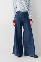 Jean de corte wide leg con tiro alto, confeccionado en denim azul oscuro. Presenta costuras verticales a lo largo de las piernas con pespuntes en color verde a contratono.