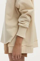 Buzo de felpa liviana color beige, con mangas largas, cuello redondo y bordado artesanal en el pecho.
