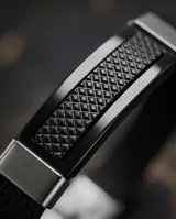 Pulsera de diseño masculino con banda de cuerina negra y placa central de acero con textura geométrica y detalles laterales en acero pulido.