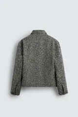 Sobrecamisa de corte relajado con textura de tejido estructurado en color gris y negro. Presenta cuello clásico, cierre frontal con botones, mangas largas con puños abotonados y bolsillos de plastrón en el pecho.
