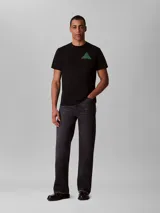 Remera de algodón negro con cuello redondo y mangas cortas. Presenta un diseño gráfico geométrico en forma de pirámide compuesto por las siglas CK en color verde en el pecho.