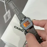 Reloj digital Casio estilo vintage con caja plateada de 28mm y correa de cuero gris con textura de cocodrilo. Cuenta con pantalla digital, funciones de cronómetro, alarma y calendario.