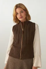 Chaleco corto entallado de lana fina sin teñir, color marrón claro jaspeado, con cierre frontal y alforzas verticales en delantera y espalda.