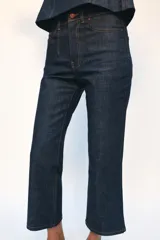 Jeans de tiro medio con corte cropped flare, confeccionados en denim azul oscuro. Presentan diseño de cinco bolsillos, trabillas en la cintura, raya planchada en el delantero y bajo con acabado evasé. Cierre frontal con cremallera y botón metálico.
