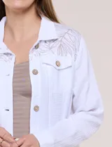 Camperita corta de calce recto color blanco, confeccionada en tejido liviano con textura arrugada. Cuenta con cuello con solapa, diseño estampado sobre los hombros y canesú, cierre frontal con botones de madera rústicos, bolsillos superiores en el pecho con solapa y mangas largas con puño abotonado.