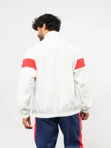 Buzo deportivo de nylon con medio cierre frontal y cuello alto. Presenta un diseño de bloques de color en azul, blanco y bordó, con el escudo del Club Nacional de Football y el logo de Umbro en el pecho.