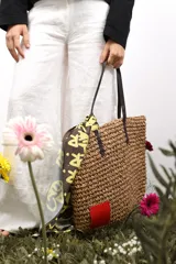 Bolso de rafia color beige con asas de cuero marrón y parche rojo en una esquina.