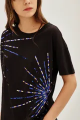 Remera negra de manga corta con cuello redondo, decorada con apliques de lentejuelas azules y doradas dispuestas en forma de explosión o rayos.